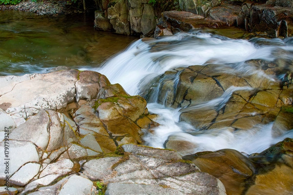 Fototapeta A mountain stream among pebbles with small waterfalls