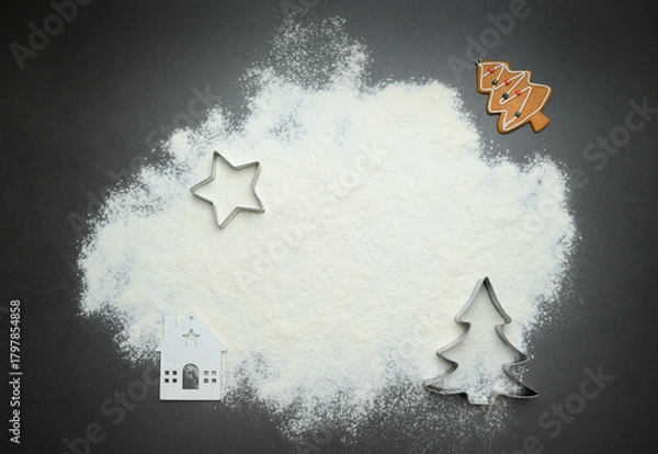 Fototapeta A dark Christmas background with scattered flour and cookie cutters shaped like a tree and star, creating a clean festive frame for holiday baking themes, decorative seasonal layouts, winter marketing