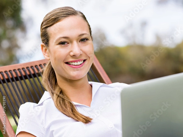 Fototapeta Young business woman sitting in park and working with laptop