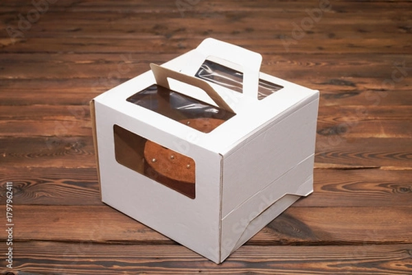 Obraz  Delicious chocolate cake in a white folding cardboard box on wooden boards.