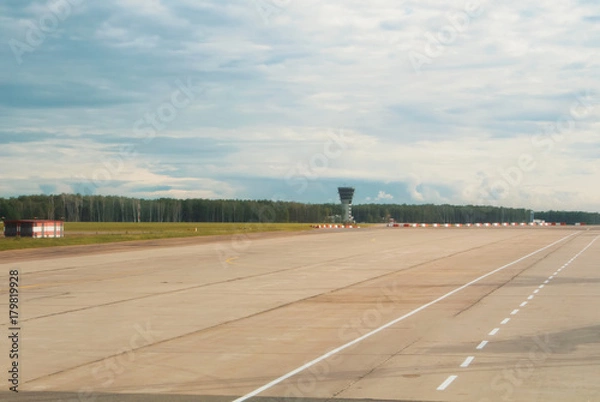 Fototapeta Airport runway with a forest at the background on cloudy day.