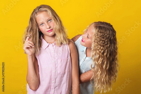 Fototapeta Funny girls twins have fun together on yellow background.