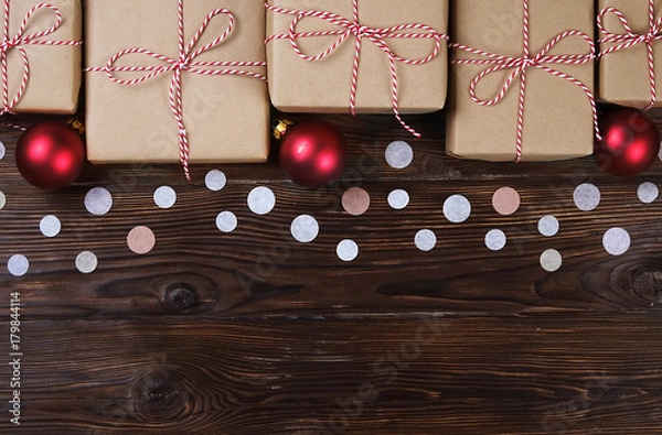 Fototapeta Lots of gift boxes on wooden background with confetti. Stylish presents in craft paper decorated with striped red and white ribbon bows. Christmas and winter holidays concept, top view, flat lay