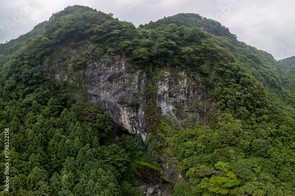 Obraz A dramatic, aerial view of a dark, rocky mountain covered in lush green vegetation. The scene evokes a sense of rugged beauty and isolation.