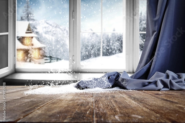 Obraz Wooden table with free space for your product or promotional text. Open window with snowfall. Landscape of winter forest mountains and small dock at the end of the village.