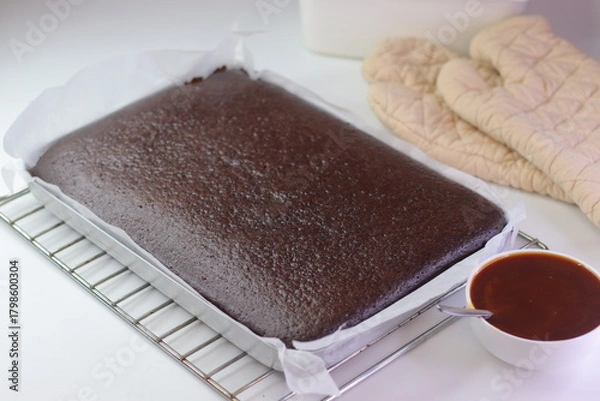 Fototapeta Freshly baked chocolate sheet cake in a parchment lined tray resting on a wire cooling rack