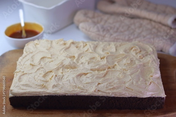 Fototapeta Chocolate sheet cake with a thick layer of buttercream frosting placed on a wooden cutting board