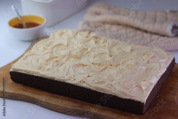 Fototapeta Chocolate sheet cake with a thick layer of buttercream frosting placed on a wooden cutting board