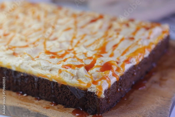 Fototapeta Chocolate sheet cake with a thick layer of buttercream frosting, drizzled with caramel cream sauce