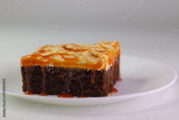 Fototapeta Moist chocolate cake slice topped with buttercream frosting and drizzled with caramel cream sauce.