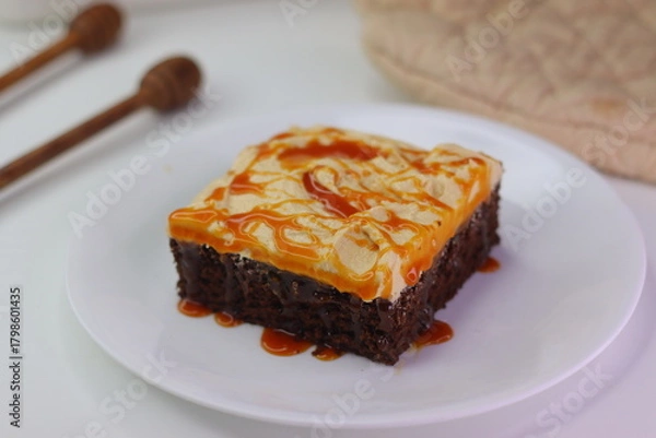 Fototapeta Moist chocolate cake slice topped with buttercream frosting and drizzled with caramel cream sauce.