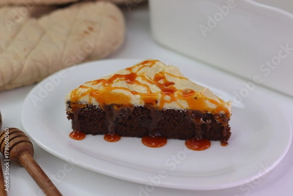Fototapeta Moist chocolate cake slice topped with buttercream frosting and drizzled with caramel cream sauce.