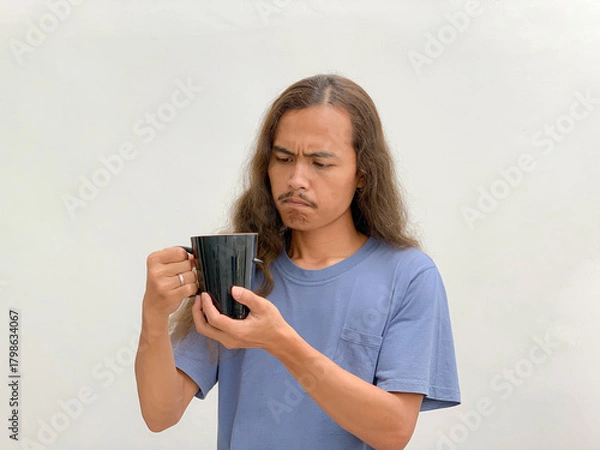 Fototapeta long-haired man holding and looking at a cup