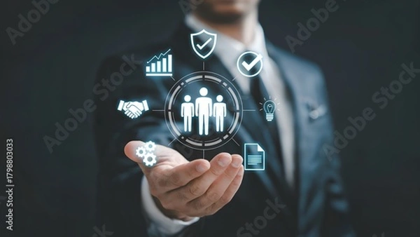 Fototapeta A businessman in a suit holding out a hand with glowing digital overlays showing teamwork icons analytics security and innovation in a dark workspace