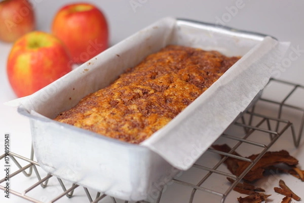 Fototapeta Freshly baked apple cinnamon bread loaf in a parchment lined metal pan on a cooling rack