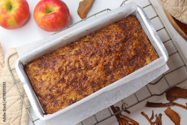 Fototapeta Freshly baked apple cinnamon bread loaf in a parchment lined metal pan on a cooling rack