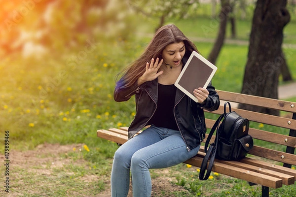 Fototapeta Young girl in the park with a tablet in hand.