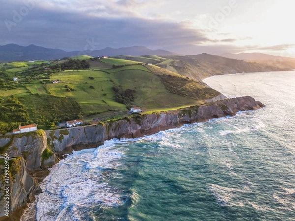 Obraz Aerial view of the Atlantic coastline with steep cliffs, green hills, and waves breaking at sunset, Basque Country, Spain