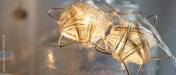 Fototapeta Lumière chaude d'une guirlande en fil de fer en forme d'étoile, allumée en décoration dans un intérieur, réchauffant l'ambiance bleutée du soir, format bannière