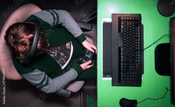 Fototapeta Entertainment, home electronics, gaming concept: a teenager boy playing computer video game with wireless controller gamepad late at night