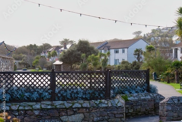 Fototapeta A peaceful view shows a well-kept park with stone walls and a wooden fence, backed by houses on a gentle hil in Perranporth - Cornwall - UK