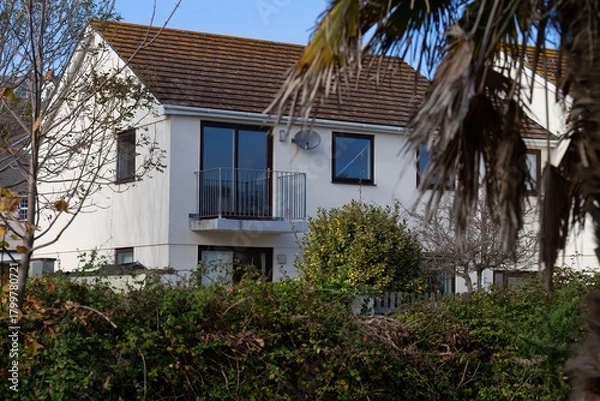 Obraz A white house with a brown roof viewed through greenery in Perranporth - Cornwall - UK