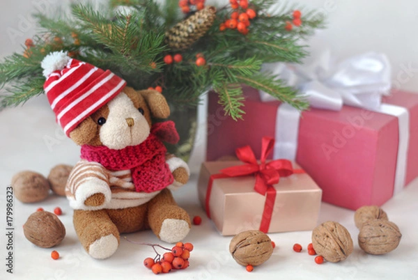 Obraz A small  toy dog in a knitted cap, gift boxes, nuts and Christmas spruce branches. Christmas and New Year card. Still life.
