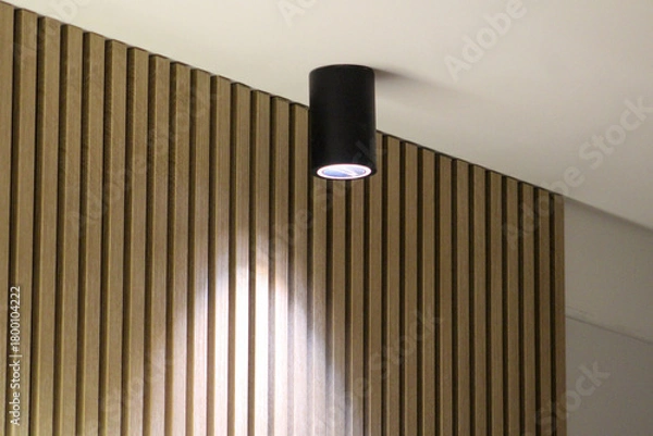 Obraz Modern ceiling spotlight illuminating a wooden slat wall, highlighting texture and minimalistic interior design with warm and soft lighting.
