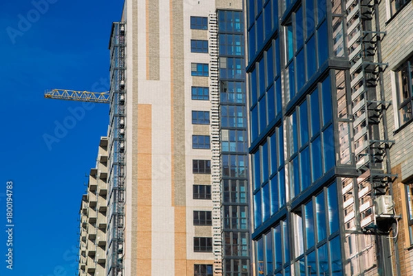 Fototapeta Modern residential buildings are being built with cranes in the foreground against a bright blue sky, highlighting the city's growth and construction activity. High quality photo