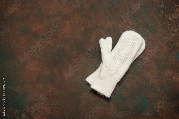 Fototapeta White knitted mittens on dark brown grunge background, top view, flat lay, copy space