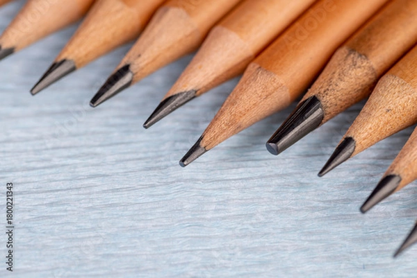 Fototapeta wooden pencils with black lead on blue corrugated paper, several monochrome pencils for sketches or graphic work are in a row.