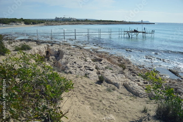 Fototapeta Coastal view with rocky shoreline and wooden pier under bright sky, serene nature landscape, copy space