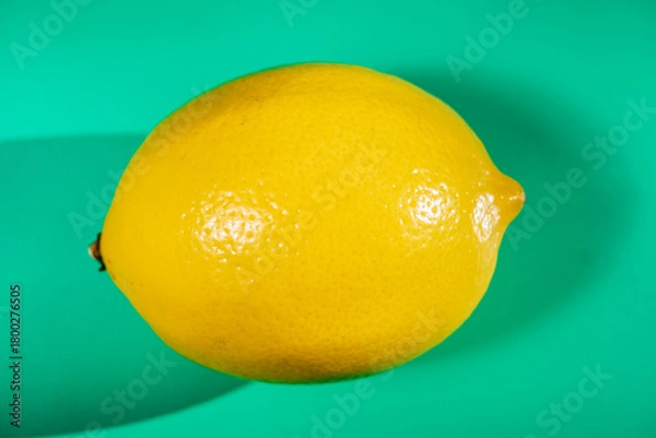 Fototapeta A vibrant yellow lemon resting on a table, captured in soft natural light. The image highlights the fruit’s bright color, fresh texture, and simple composition, making it suitable for food photography