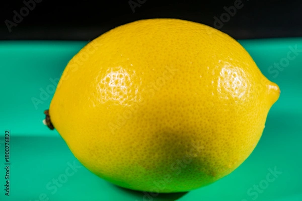 Fototapeta A vibrant yellow lemon resting on a table, captured in soft natural light. The image highlights the fruit’s bright color, fresh texture, and simple composition, making it suitable for food photography
