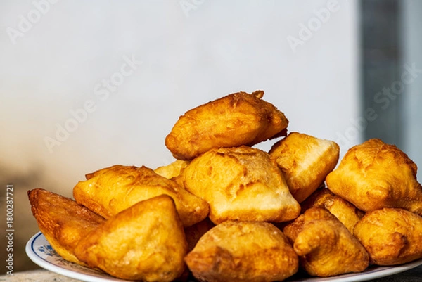 Fototapeta Golden, freshly fried fritters arranged on a plate, featuring a crispy exterior and a soft, airy inside. Warm lighting enhances their rich golden color and homemade rustic appearance. 