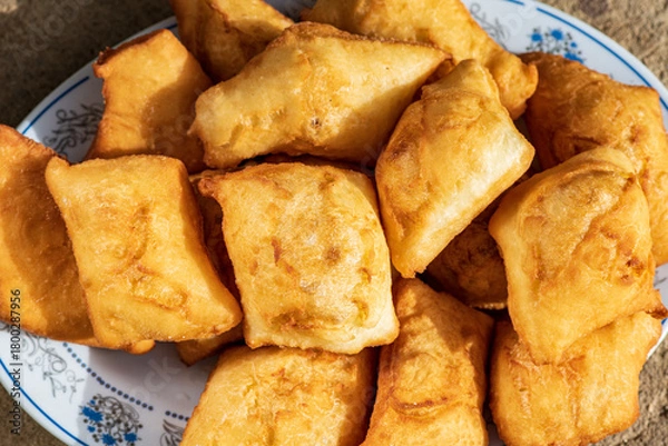 Fototapeta Golden, freshly fried fritters arranged on a plate, featuring a crispy exterior and a soft, airy inside. Warm lighting enhances their rich golden color and homemade rustic appearance.