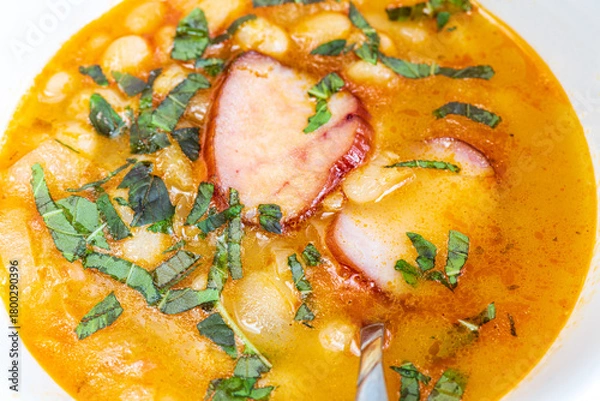 Fototapeta A hearty bowl of cooked bean stew with tender pieces of meat, served in a clean white dish. The warm, rich broth highlights the soft beans and juicy meat, while natural lighting 