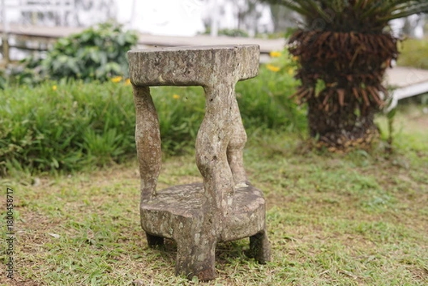 Obraz Rustic stone stool featuring a unique, weathered design and intricate carvings, standing elegantly on green grass in a tranquil outdoor garden setting