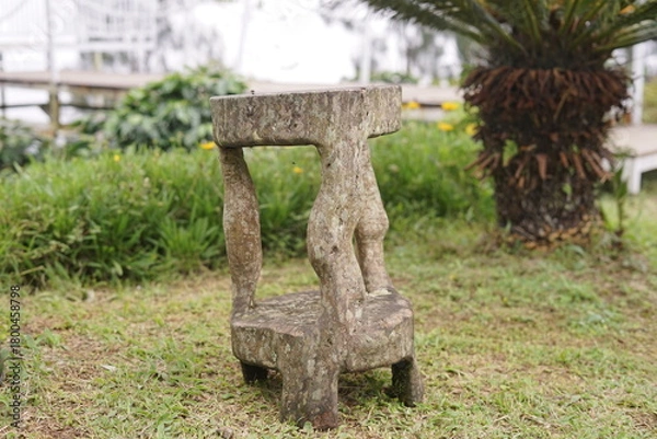Obraz Weathered wooden stool with an organic, rustic design stands amidst green grass in a tranquil garden setting, offering a touch of natural artistry and unique outdoor decor