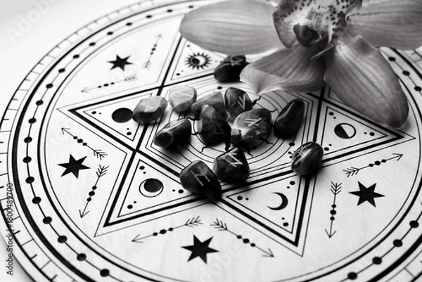 Fototapeta Scandinavian amethyst runes on a wooden altar for divination and an orchid flower. Black and white photo. Fortune telling, witchcraft, and spiritual esoteric practice.