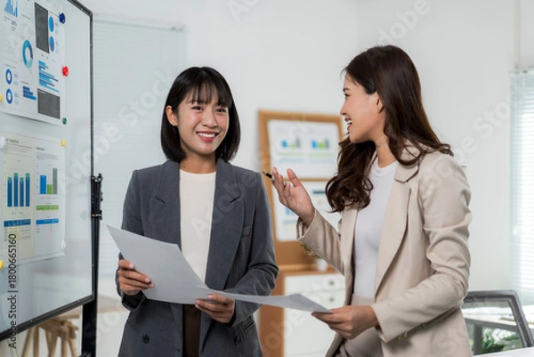 Fototapeta Two asian businesswomen discussing charts and data during a corporate meeting