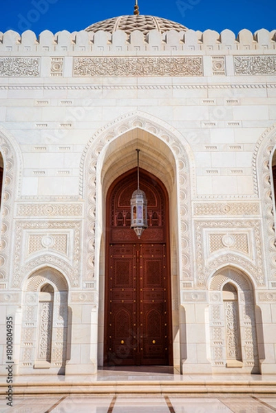 Fototapeta A striking architectural photograph showcasing an ornate wooden entrance door framed by an intricately carved marble archway at the Sultan Qaboos Grand Mosque in Muscat, Oman