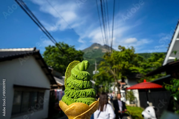 Fototapeta Enjoy authentic local green tea ice cream soft serve cone on the street on spring day with blurred people, mountain and blue sky background