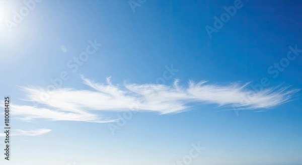 Fototapeta A serene blue sky with wispy white clouds and a bright sun shining down.