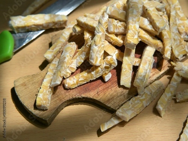 Fototapeta Raw tempeh slices in stick form on a wooden cutting board. Preparing to cook tempeh. Preparing to eat tempeh.