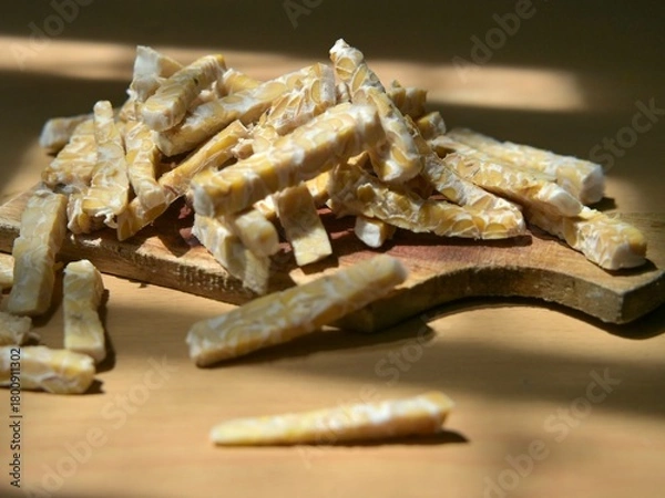 Fototapeta Raw tempeh slices in stick form on a wooden cutting board. Preparing to cook tempeh. Preparing to eat tempeh.