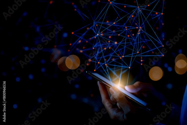 Fototapeta A hand holds a smartphone, illuminated by digital connections and glowing nodes, set against a dark background, symbolizing technology and communication.