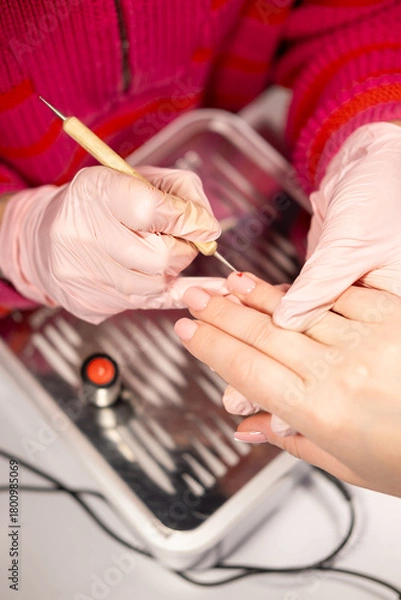 Fototapeta Manicure treatment. Spa therapy. Beauty master hands in pink protective latex gloves drawing acrylic color varnish on nail tip with tool female client care salon routine.
