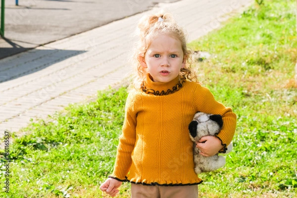 Obraz Caucasian girl with curly hair holding a stuffed animal outdoors. Child playtime and toy companionship concept for early childhood development.