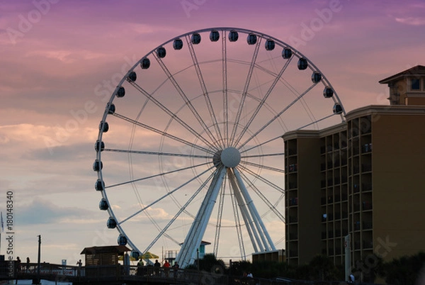 Fototapeta A large ferris wheel in down Myrtle Beach, South Carolina as the sun sets against a purple sky.
